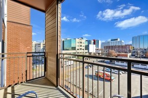 Een balkon met uitzicht op een stadsbeeld, inclusief moderne gebouwen en een parkeerplaats.