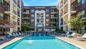 Ein modernes Apartmenthaus mit einem zentralen Schwimmbecken, Liegestühlen und Außenmöbeln.