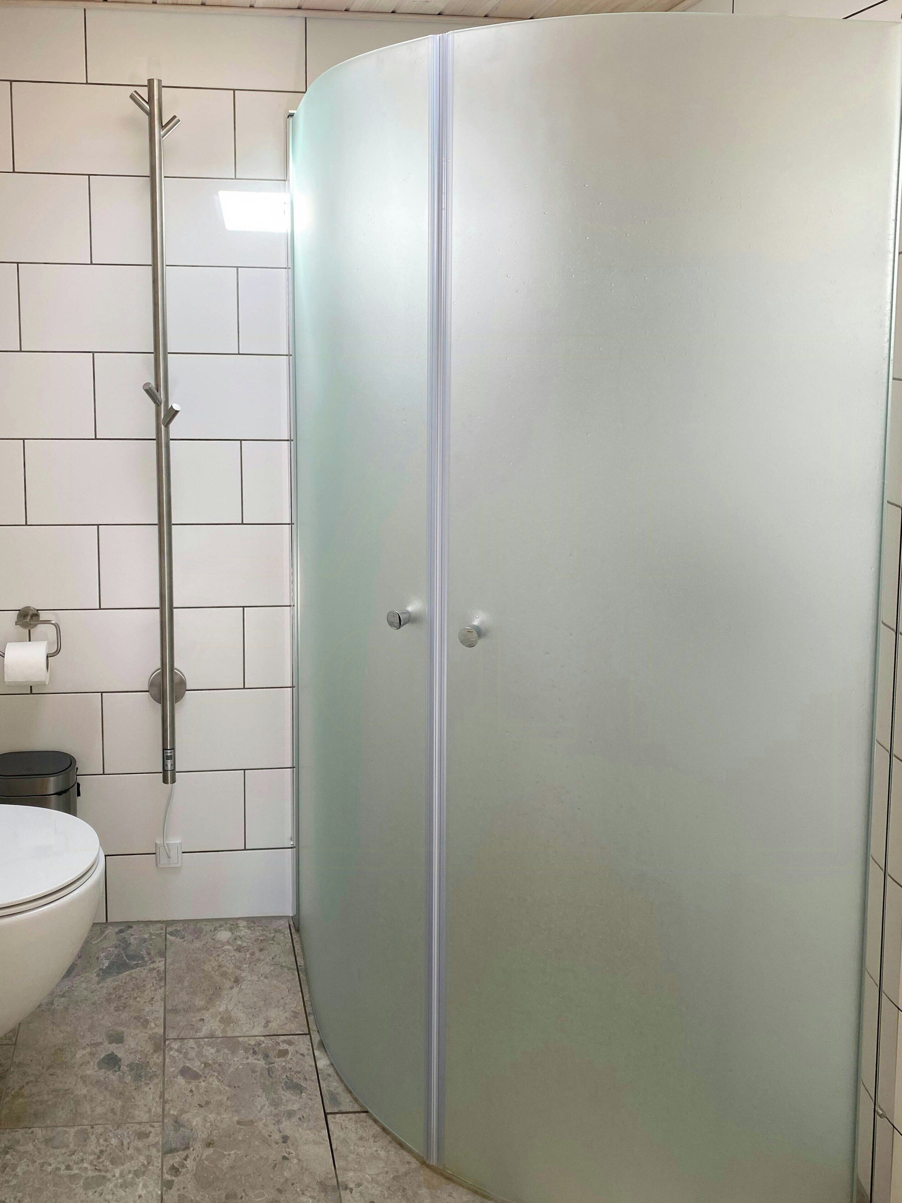 Et badeværelse med toilet, brusebad og en brusekabine med glasvægge.
