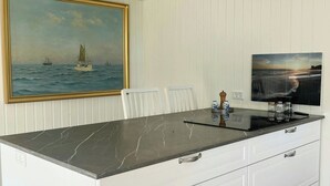 Ett kök med en bänkskiva i marmor, vita skåp och en tavla som föreställer en segelbåt på väggen.