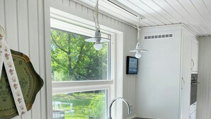 Ett kök med en svart bänkskiva i marmor, vita skåp, ett fönster med utsikt över grönområden och en hängande lampa.