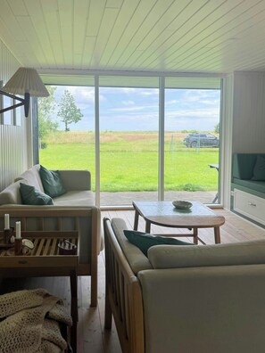 Ein Zimmer mit einer Couch, einem Tisch und Blick auf ein grünes Feld durch große Fenster.