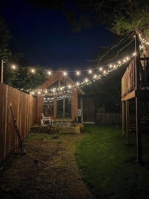 Un patio trasero con terraza de madera, un porche cubierto y luces colgantes.