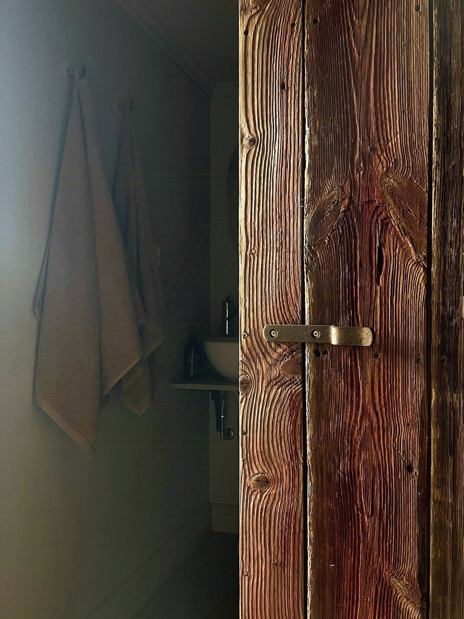 Una puerta de madera con un pestillo metálico, una toalla colgada en la pared y un estante con objetos.