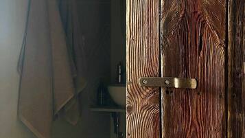Una puerta de madera con un pestillo metálico, una toalla colgada en la pared y un estante con objetos.