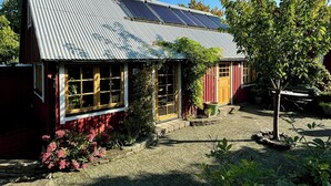 A house with a corrugated metal roof, solar panels, a red door, and a garden with potted plants. - Charming cottage in scenic Brösarp Österlen (Kivik)