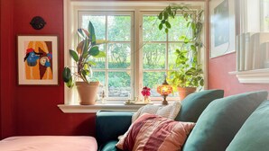 A cozy room with a teal sofa, a pink ottoman, and a window with plants. - Charming cottage in scenic Brösarp Österlen (Kivik)