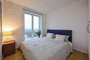 Quarto com cama, janela, mesa de cabeceira e um vaso com planta.