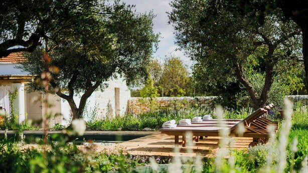 Un patio in legno con poltroncine da relax e asciugamani, immerso nel verde e alberi.