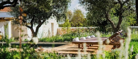 Una terraza de madera con sillones de descanso y toallas, rodeada de follaje y árboles.
