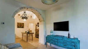 Un soggiorno con un divano, un comò color petrolio, una TV montata a parete e una porta ad arco che conduce a una sala da pranzo.