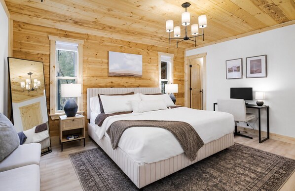 A bedroom with a large bed, bedside tables, a desk with a chair, a television, and a window.
