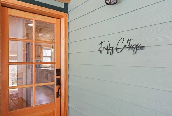 A wooden door with glass panels and a wall sign that reads 'Firefly Cottage EST 2023.'