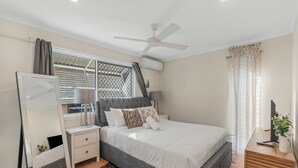 Un dormitorio con cama, mesitas de noche, un espejo, ventilador de techo y ventana con cortinas.