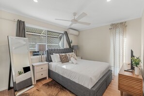 Ein Schlafzimmer mit Bett, Nachttischen, einem Spiegel, einem Deckenventilator und einem Fenster mit Vorhängen.