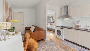 Un espacio habitable compacto con kitchenette, sofá, lavadora y cama al fondo.