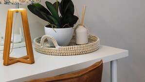 Una mesa blanca con una planta en maceta, una lámpara y una bandeja tejida.