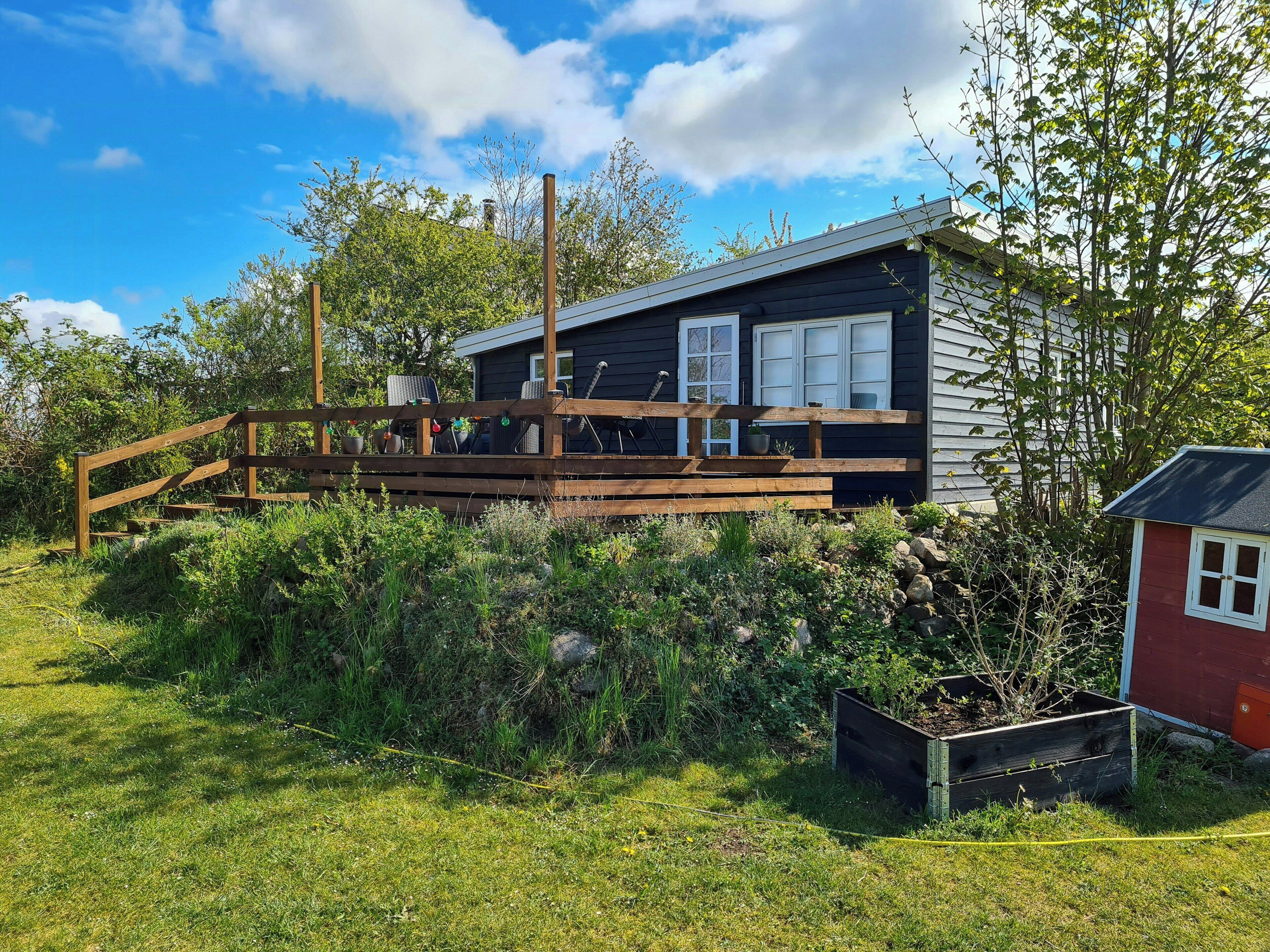 A cabin with a wooden deck, a small garden, and a red shed.