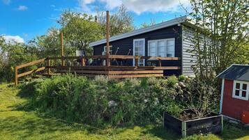 A cabin with a wooden deck, a small garden, and a red shed.