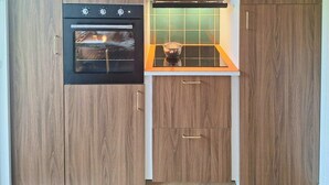Une cuisine compacte dotée d’un four encastré, d’un petit plan de travail et de meubles de rangement en bois.