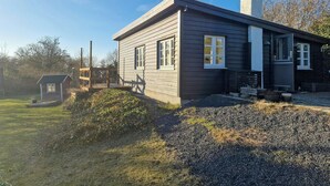 Une maison à deux étages avec une cheminée, une petite terrasse et une allée gravillonnée.