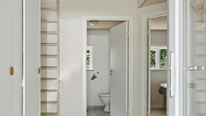 Un couloir avec un plafond en bois, un escalier et une salle de bain visible à travers une porte ouverte.