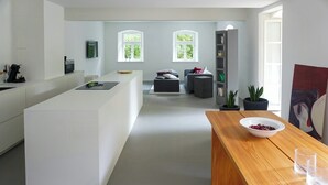 A modern kitchen with a central island, a dining table with a bowl and glasses, and a bookshelf with plants. - Design apartment in the historic Mittermurnthal (Neunburg vorm Wald)