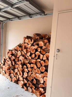 A stack of firewood in a garage with a metal roof and a beige wall. - Alpine Luxe Cardrona (Cardrona)