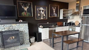A modern kitchen with a stone fireplace, a dining table, and artwork on the wall. - Alpine Luxe Cardrona (Cardrona)