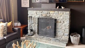 A modern living room with a stone fireplace, a flat-screen TV mounted above it, and a cozy seating area with a sofa and a coffee table. - Alpine Luxe Cardrona (Cardrona)
