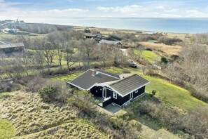Ein modernes Haus mit Satteldach, umgeben von einer grünen Landschaft und Blick auf das Meer.