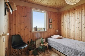 Ein Zimmer mit Holzwänden, einem Bett, einem Stuhl, einem Fenster und einer Pendelleuchte.