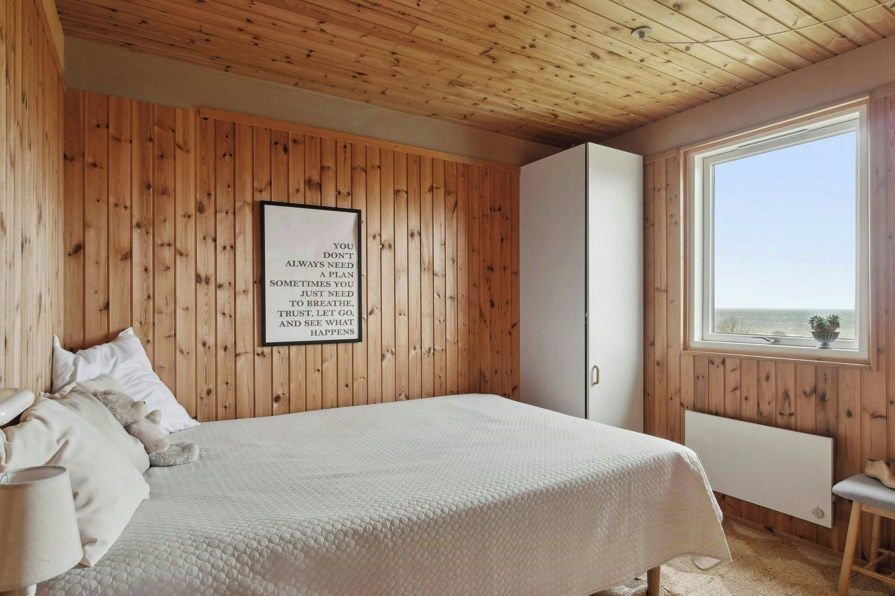 Camera da letto con pareti in legno, un letto, una finestra vista e una citazione motivazionale sulla parete.