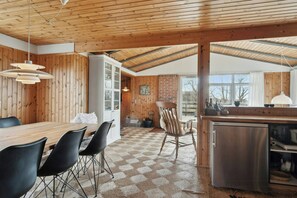 Eine moderne Küche mit Holzwänden, ein Essbereich mit Holztisch und -stühlen sowie ein Blick durch das Fenster.