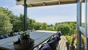 Um deck de madeira com mesa e cadeiras, rodeado por vegetação exuberante e vista para a paisagem.