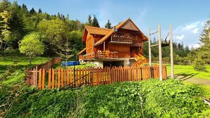 Uma cabana de madeira com varanda, cercada por uma vedação de madeira e vegetação exuberante.
