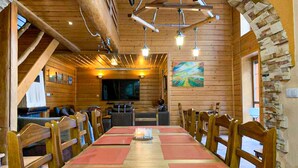 Interior de madeira com uma longa mesa de jantar, cadeiras, uma televisão e um quadro na parede.