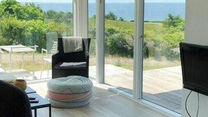 A modern living room with a large glass door leading to a balcony with a view of the sea.