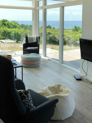 A modern living room with a large glass door leading to a balcony with a view of the sea.