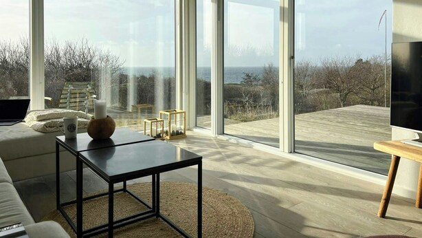A modern living room with large glass doors leading to a balcony, a sofa, a coffee table, and a TV.