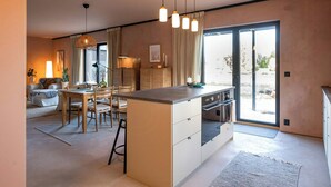 A modern kitchen with a central island, dining area, and a large sliding glass door to the outdoors.