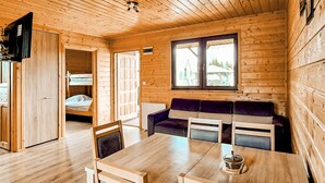 Een houten blokhut van binnen, met een eettafel, stoelen, een bank en een stapelbed.