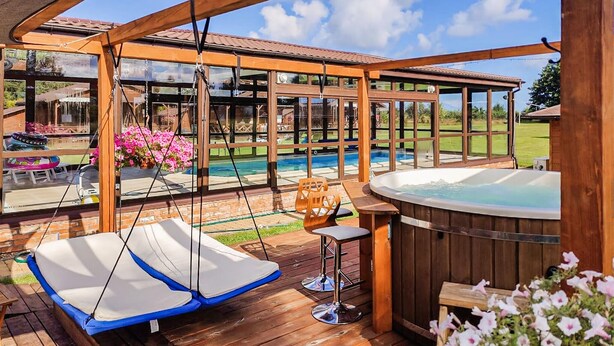 Een houten terras met een jacuzzi, een hangstoel en uitzicht op het zwembad.
