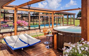 Een houten terras met een jacuzzi, een hangstoel en uitzicht op het zwembad.