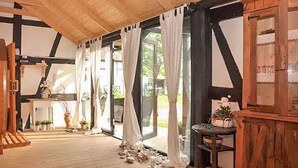 A room with a wooden ceiling, large windows with curtains, a wooden table with a vase, and a door with a window. - Amazing home in Jaroslawiec with sauna (Jaroslawiec)