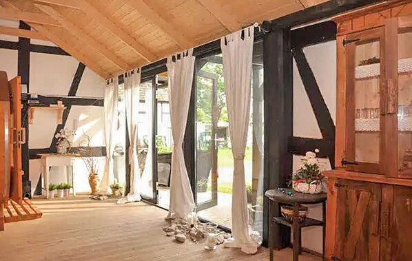 A room with a wooden ceiling, large windows with curtains, a wooden table with a vase, and a door with a window.
