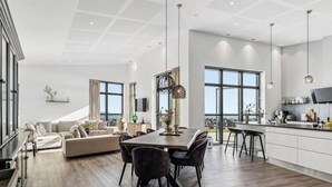 Ampla sala de estar com mesa de jantar, sofás e área de cozinha com uma janela grande.