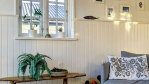Une pièce avec une fenêtre, une table en bois ornée de plantes, un canapé gris et des tableaux accrochés au mur.