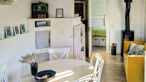 Un salon chaleureux avec une table de salle à manger ronde, des chaises blanches, un canapé et un poêle à bois.