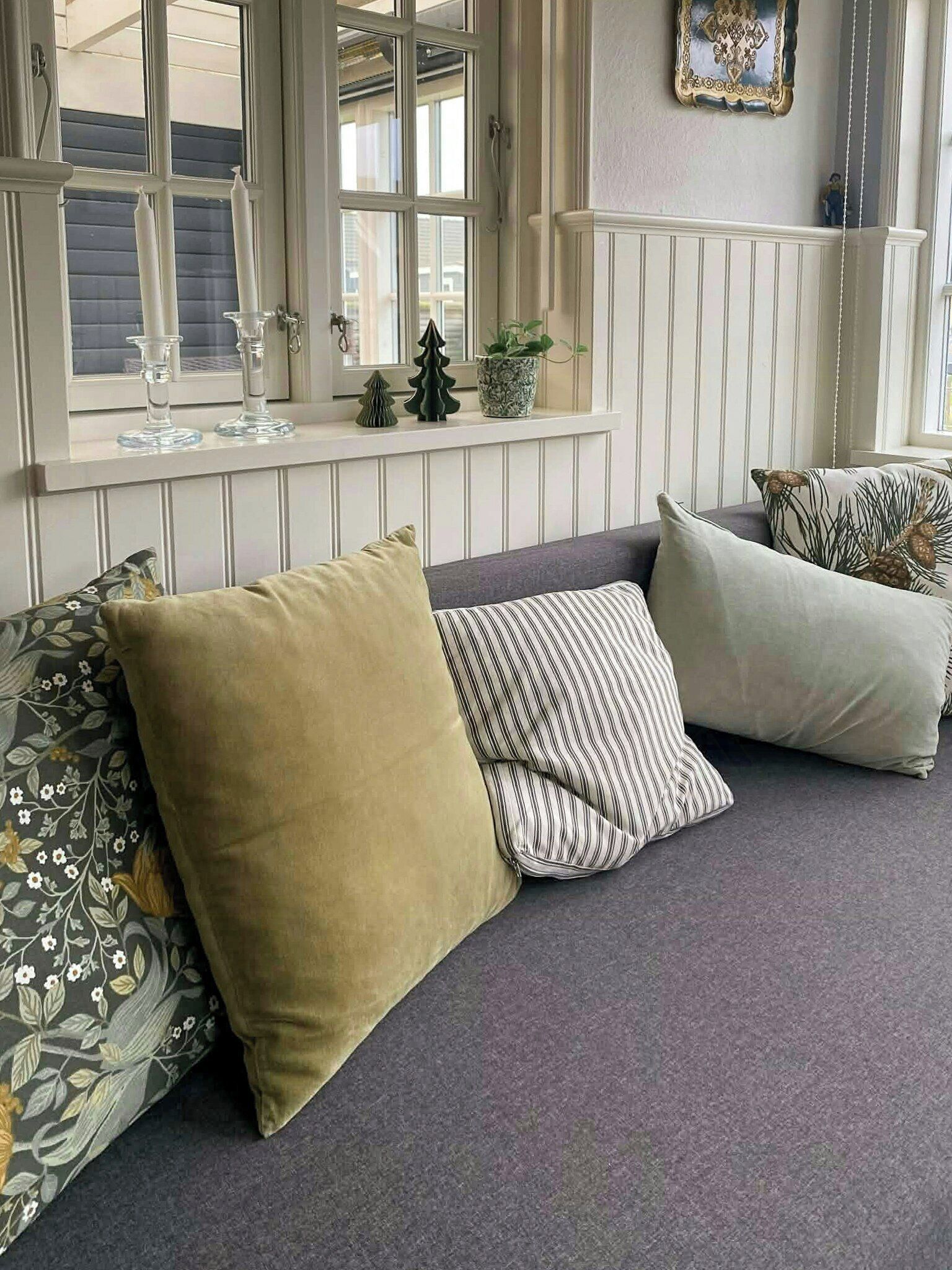 Una zona de estar con un banco acolchado, cojines decorativos, una ventana con vistas y una planta pequeña en el alféizar.